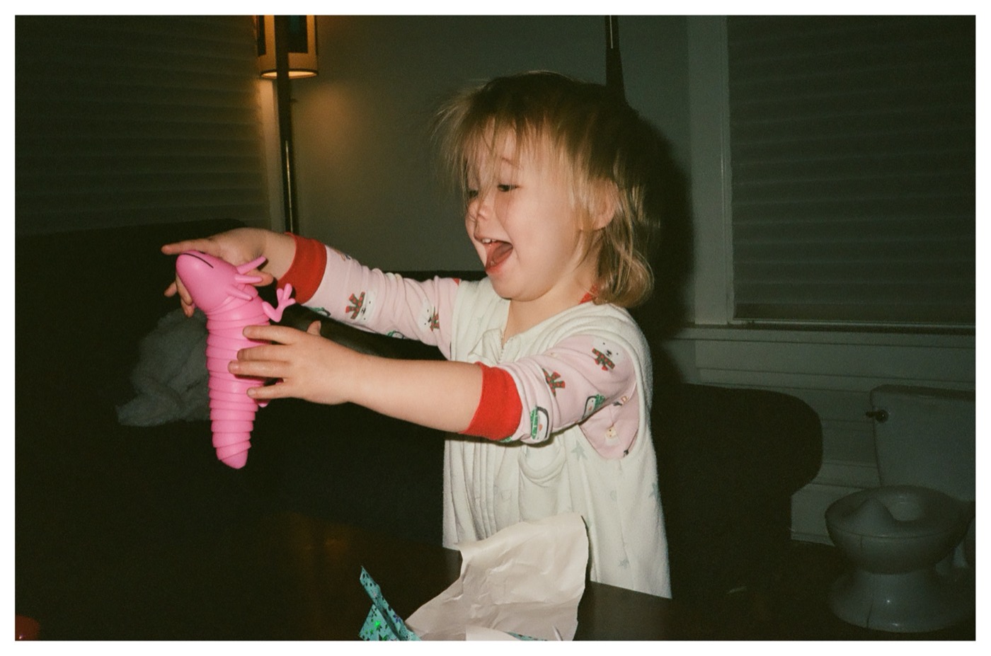 Lily in Christmas pajamas, laughing and holding up a pink toy