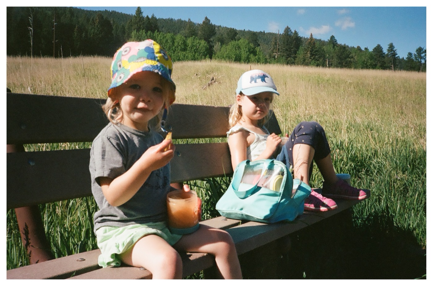 Lily and a friend snacking on a bench in a mountain meadow
