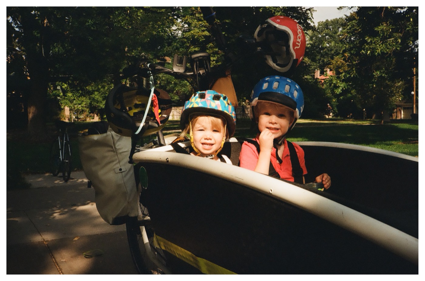 Lily and a friend in helmets, riding in the front of a cargo bike